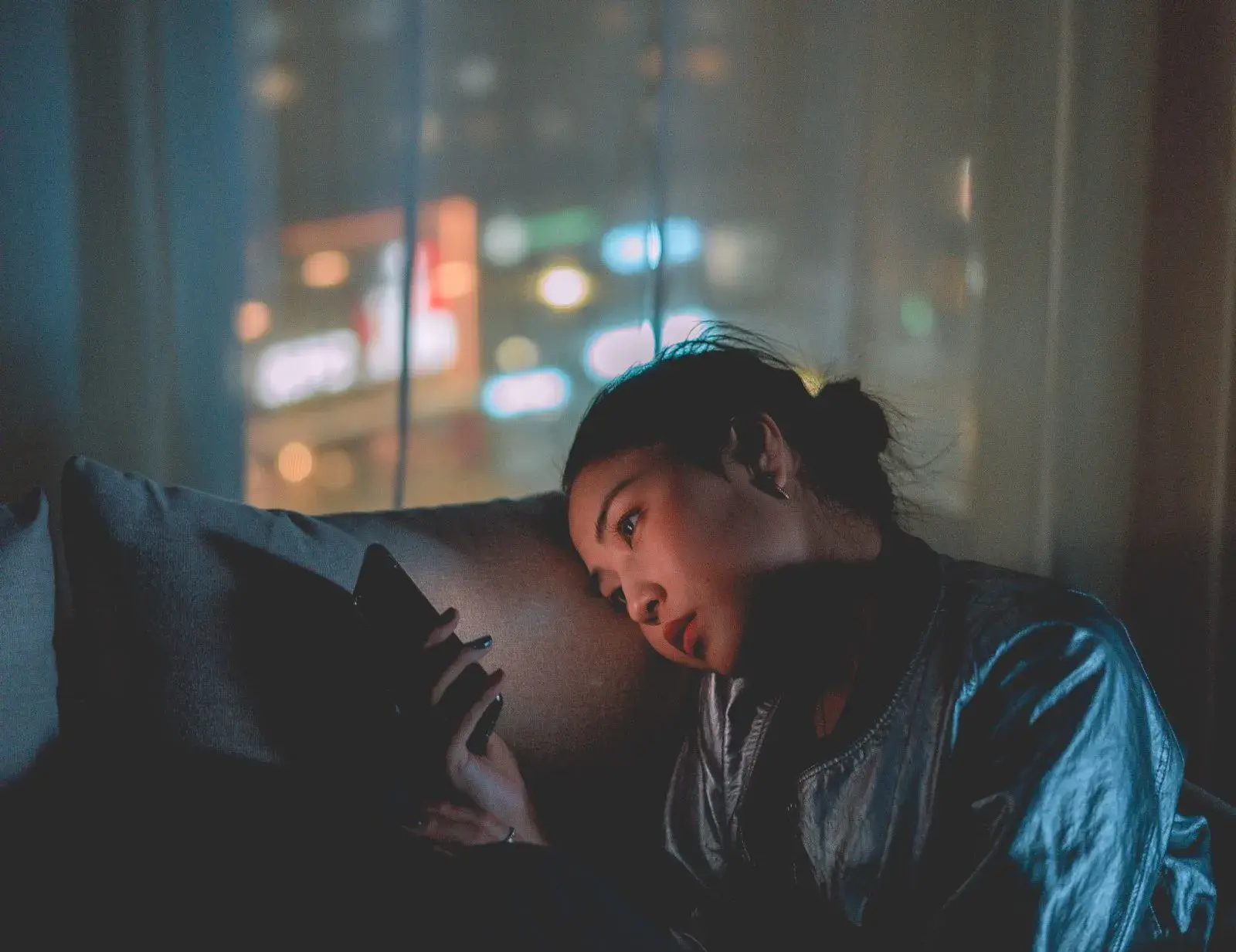 A woman lying on a couch looking at her phone late at night
