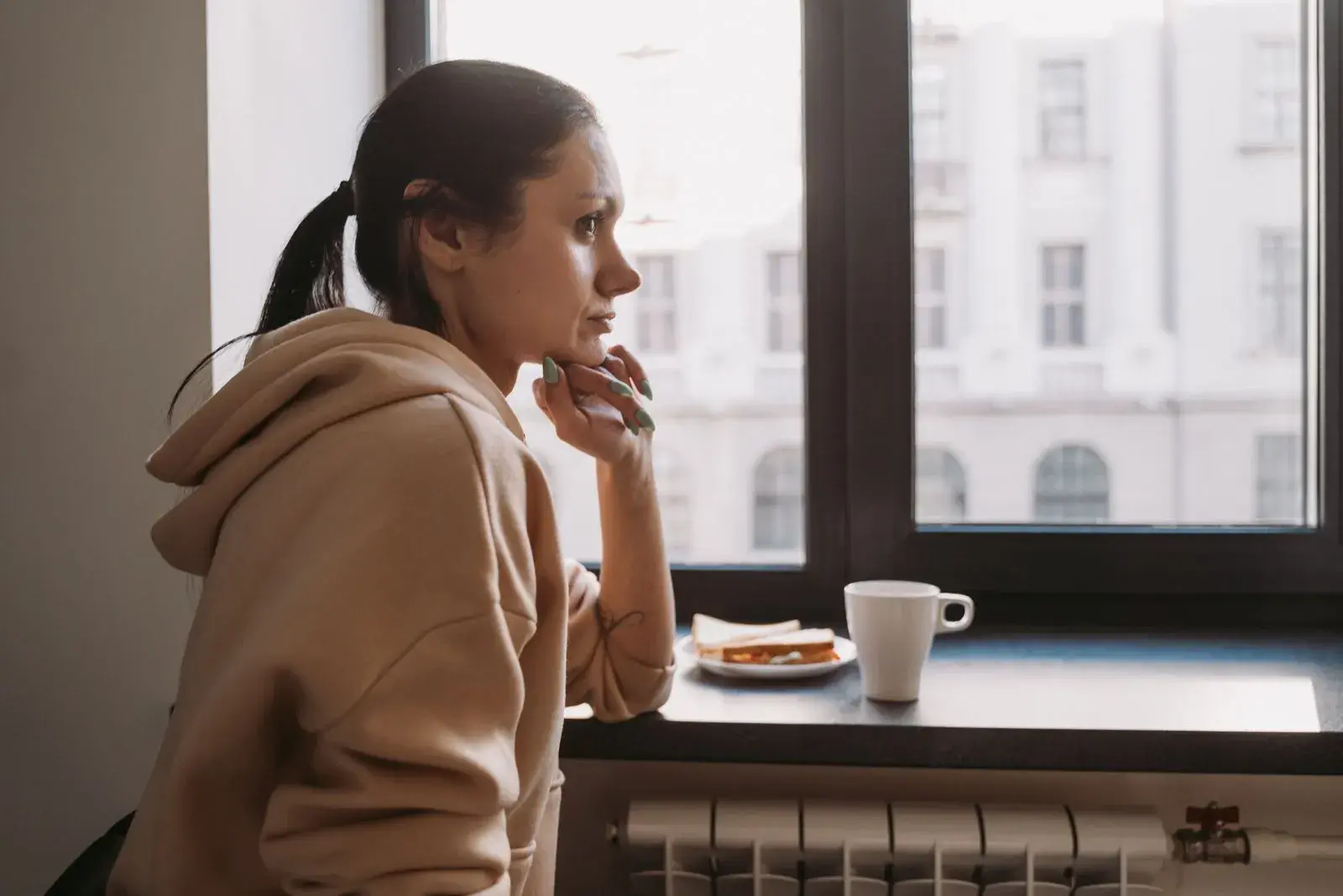 A woman looking thoughtfully out of a window with a cup of coffee